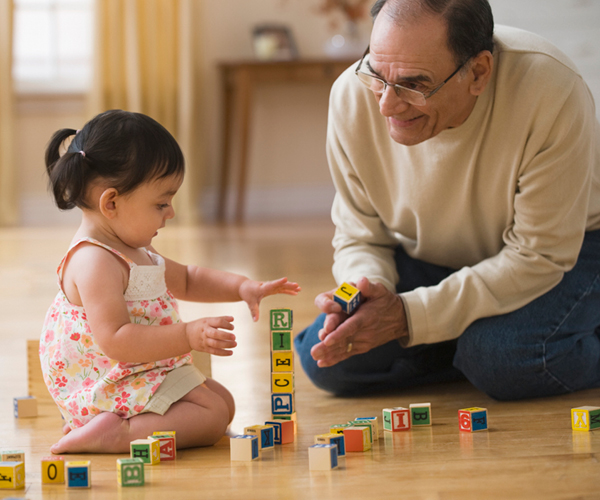 Imagen de un abuelo sonriendo a un niño jugando con bloques de alfabeto.