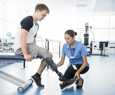 Un proveedor de salud, agachado en el suelo, ajusta la prótesis de pierna de un hombre.