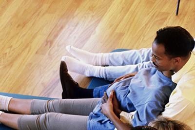 Una mujer embarazada y su pareja se sientan juntos en una colchoneta durante una clase de preparación para el parto.