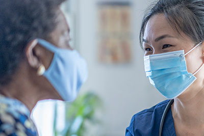 Una mujer habla con un profesional de la salud en una sala de exámenes. Ambas personas llevan mascarillas.