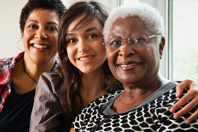 Tres mujeres sonrientes de distintas generaciones con una familia.